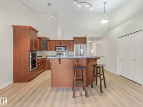 The kitchen features rich wood cabinetry, stainless steel appliances, and a breakfast bar - 515 10311 111 Street, Edmonton, AB - Indoor Photo Showing Kitchen