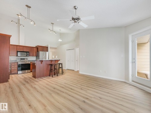 Open concept living area featuring light-toned flooring, a ceiling fan, and a door leading to an outdoor space - 515 10311 111 Street, Edmonton, AB - Indoor Photo Showing Kitchen
