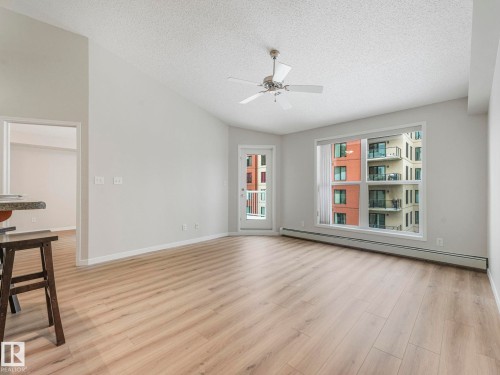 The living area features light wood-style flooring, a large window, a glass patio door, and a ceiling fan - 515 10311 111 Street, Edmonton, AB - Indoor