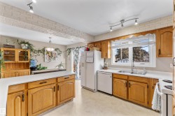 Kitchen with brown cabinets, light countertops, white appliances, track lighting, and hanging light fixtures - 
