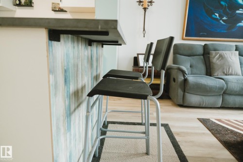 The property features an extended countertop with a decorative panel, light-colored flooring, and a living area with a sofa - 303 10432 76 Avenue, Edmonton, AB -  With Exterior