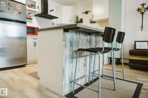 Kitchen featuring an island with a breakfast bar, white cabinetry, a stainless steel refrigerator, and light-toned flooring - 303 10432 76 Avenue, Edmonton, AB - Indoor Photo Showing Other Room