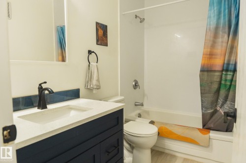 The bathroom features a vanity with a white countertop and a dark blue base, a white toilet, and a bathtub with a shower - 303 10432 76 Avenue, Edmonton, AB - Indoor Photo Showing Bathroom