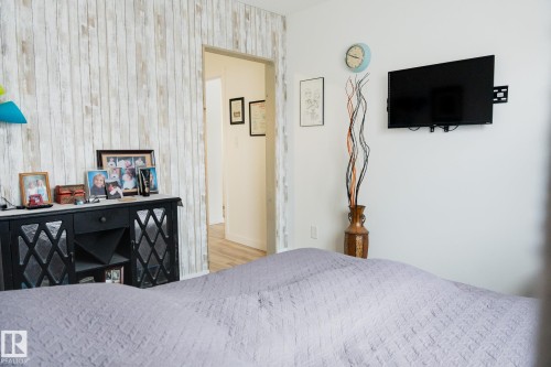 This room features a white wall with a mounted television and a decorative accent wall with a wood plank design - 303 10432 76 Avenue, Edmonton, AB - Indoor Photo Showing Bedroom