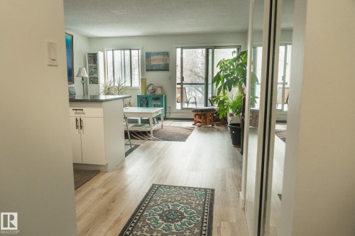 Entryway featuring light-toned flooring, leading towards a living area with large windows providing natural light - 303 10432 76 Avenue, Edmonton, AB - Indoor Photo Showing Other Room
