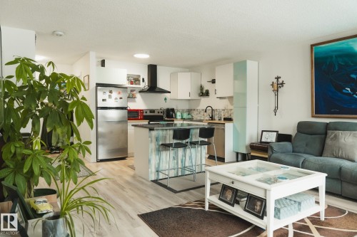 The open-concept living area features light-toned flooring, a kitchen island with seating, and a modern kitchen with white cabinetry and stainless steel appliances - 303 10432 76 Avenue, Edmonton, AB - Indoor