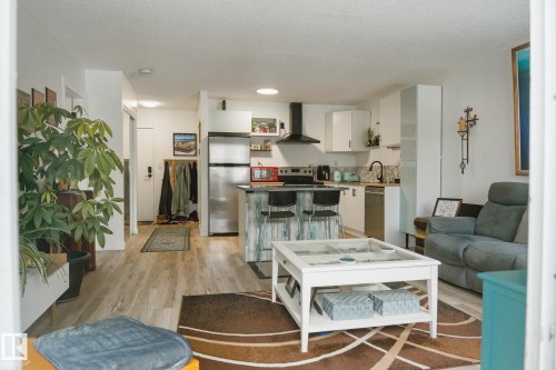 Open concept living area featuring light-toned flooring, a kitchen with white cabinetry and stainless steel appliances, and a central island with seating - 303 10432 76 Avenue, Edmonton, AB - Indoor