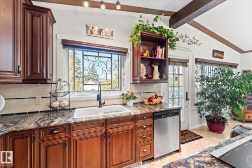 The kitchen features rich wood cabinetry, granite countertops, and a white sink with a modern black faucet - 11124 110A Avenue, Edmonton, AB - Indoor Photo Showing Kitchen With Double Sink