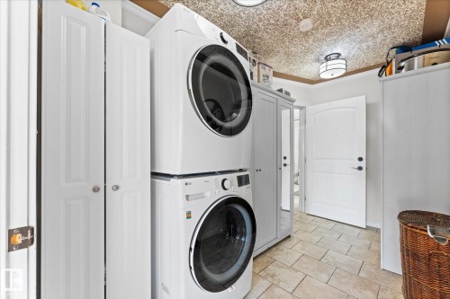 This utility space features tile flooring, a stacked washer and dryer, and white doors, including a panel door with black hardware - 11124 110A Avenue, Edmonton, AB - Indoor Photo Showing Laundry Room