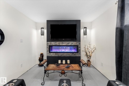 Living area featuring a wall-mounted television above an electric fireplace, set within a dark accent wall with decorative tile work - 11124 110A Avenue, Edmonton, AB - Indoor