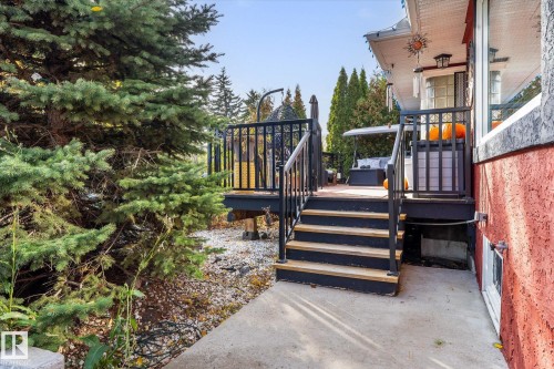 This outdoor space features a concrete pathway leading to a multi-level deck with black railings and light-colored stair treads - 11124 110A Avenue, Edmonton, AB - Outdoor