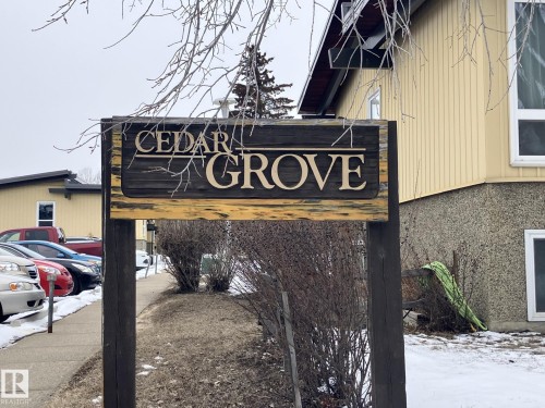 The property features a prominent wooden sign with carved lettering, set against a backdrop of light-colored siding and visible windows - 14622 118 Street, Edmonton, AB - Outdoor
