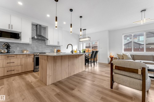 Modern open-concept living area featuring light wood flooring, a kitchen island with a light-colored countertop, and stainless steel appliances - 9 Hunter Place, Spruce Grove, AB - Indoor Photo Showing Kitchen With Upgraded Kitchen