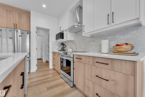 The kitchen features light wood cabinetry, white countertops, and stainless steel appliances, including a refrigerator, oven, and microwave - 9 Hunter Place, Spruce Grove, AB - Indoor Photo Showing Kitchen With Upgraded Kitchen