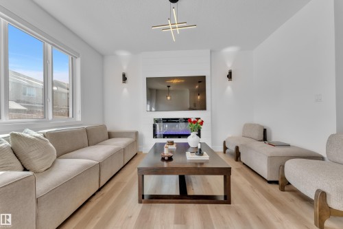 The living area features light-toned flooring, large windows providing natural light, a modern fireplace, and contemporary lighting fixtures - 9 Hunter Place, Spruce Grove, AB - Indoor Photo Showing Living Room