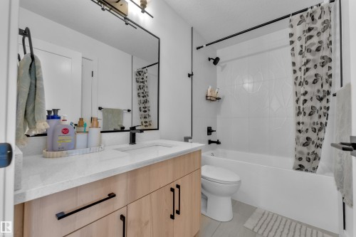 The bathroom features a modern vanity with a light-colored countertop and wooden cabinetry, a large wall-mounted mirror with a black frame, and a white bathtub with white tiled walls and black fixtures - 9 Hunter Place, Spruce Grove, AB - Indoor Photo Showing Bathroom