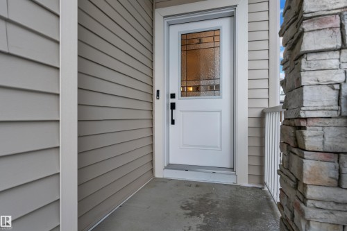 The property features a white paneled front door with decorative glass, complemented by light-colored siding and a stacked stone column - 9 Hunter Place, Spruce Grove, AB - Outdoor With Exterior