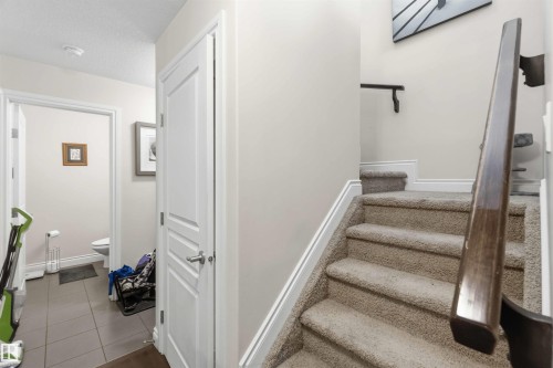 The property features a staircase with carpeted treads and a wooden handrail, alongside a hallway with tiled flooring and access to a powder room - 2037 69A Street, Edmonton, AB - Indoor Photo Showing Other Room