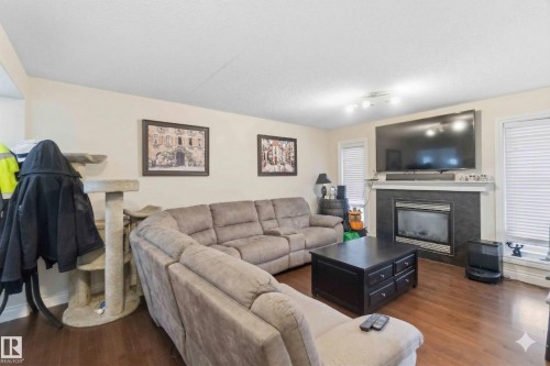 Living area featuring hardwood flooring, a fireplace with a dark tile surround and white mantel, and windows with blinds - 2037 69A Street, Edmonton, AB - Indoor Photo Showing Living Room With Fireplace