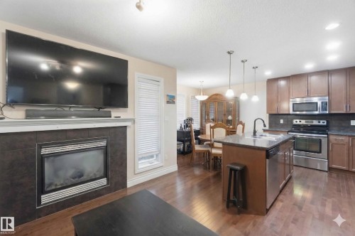 This property features an open-concept living area with hardwood flooring throughout, a fireplace with a tiled surround, and a kitchen island with a granite countertop - 2037 69A Street, Edmonton, AB - Indoor Photo Showing Other Room With Fireplace