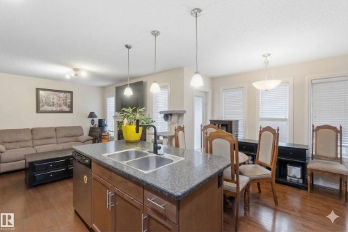 The kitchen features an island with a double sink and a stainless steel dishwasher, complemented by rich wooden cabinetry and granite-style countertops - 2037 69A Street, Edmonton, AB - Indoor Photo Showing Other Room
