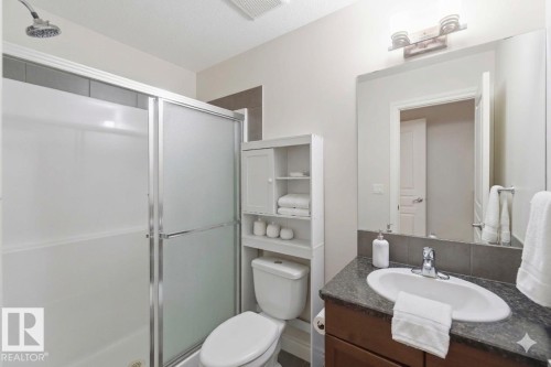 The bathroom features a shower with sliding glass doors, a vanity with a dark countertop and an undermount sink, and a mirror with overhead lighting - 2037 69A Street, Edmonton, AB - Indoor Photo Showing Bathroom