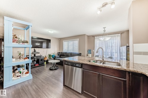 The property features an open-concept living space with dark wood flooring - 23 445 Brintnell Boulevard Nw, Edmonton, AB - Indoor Photo Showing Kitchen With Double Sink