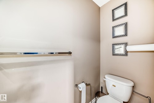 Bathroom featuring a white toilet with a beige tank lid, a chrome towel bar, and decorative framed mirrors - 23 445 Brintnell Boulevard Nw, Edmonton, AB - Indoor Photo Showing Bathroom