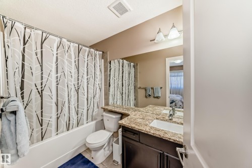 Bathroom featuring a bathtub with a shower, a toilet, and a vanity with a light-colored granite countertop and white rectangular sink - 23 445 Brintnell Boulevard Nw, Edmonton, AB - Indoor Photo Showing Bathroom