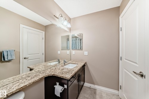 The bathroom features a double vanity with a speckled countertop, integrated sinks, and dark wood cabinetry - 23 445 Brintnell Boulevard Nw, Edmonton, AB - Indoor Photo Showing Bathroom