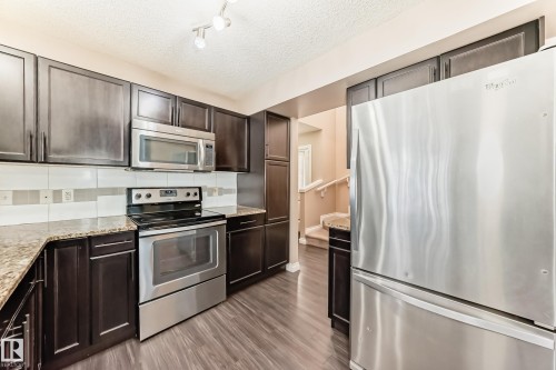 The kitchen features dark wood cabinetry, granite countertops, and stainless steel appliances including a refrigerator, stove, and microwave - 23 445 Brintnell Boulevard Nw, Edmonton, AB - Indoor Photo Showing Kitchen