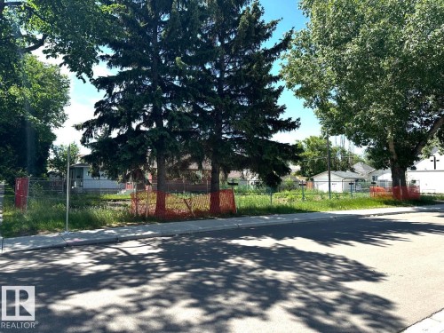 The property features mature trees, a clear parcel of land with visible fencing, and a paved road frontage with a sidewalk - 12072 95 Street, Edmonton, AB 