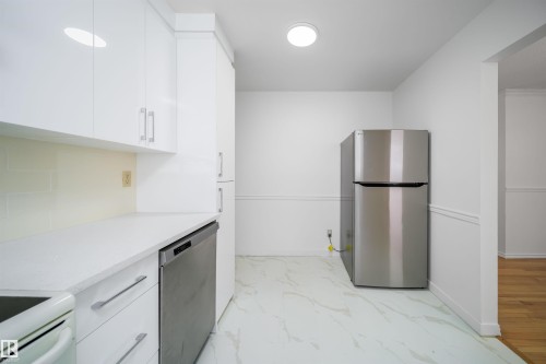 The kitchen features white cabinetry, light-colored countertops, a stainless steel refrigerator, and a stainless steel dishwasher - 6411 149 Avenue Nw, Edmonton, AB - Indoor Photo Showing Kitchen