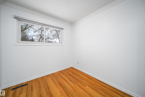 This bright room features warm-toned hardwood floors, white walls, and a window with blinds - 6411 149 Avenue Nw, Edmonton, AB - Indoor Photo Showing Other Room
