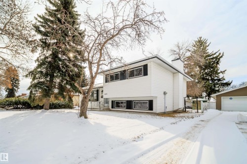The property features white siding and dark window shutters, complemented by a front yard with mature trees - 6411 149 Avenue Nw, Edmonton, AB - Outdoor