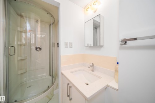 The bathroom features a glass-enclosed shower, a vanity with a white countertop and integrated sink, and a mirrored medicine cabinet - 6411 149 Avenue Nw, Edmonton, AB - Indoor Photo Showing Bathroom