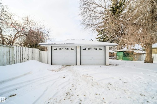 Detached garage featuring two garage doors with window accents and a white picket fence alongside the property - 6411 149 Avenue Nw, Edmonton, AB - Outdoor
