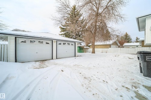 The property features a detached garage with two overhead doors, a white picket fence, and a spacious yard with mature trees - 6411 149 Avenue Nw, Edmonton, AB - Outdoor With Exterior