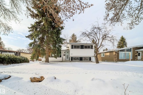 The property features a white exterior with dark window shutters, a front door with a window, and a yard with mature trees - 6411 149 Avenue Nw, Edmonton, AB - Outdoor