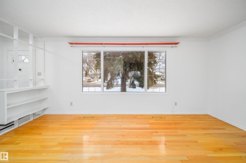 Living area featuring hardwood floors, a large window, and built-in shelving - 6411 149 Avenue Nw, Edmonton, AB - Indoor Photo Showing Other Room