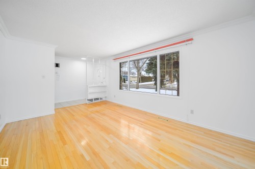 This bright living space features hardwood floors, white walls, and a large window providing views of the outdoors - 6411 149 Avenue Nw, Edmonton, AB - Indoor Photo Showing Other Room