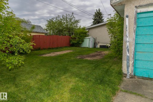 The property features a spacious yard with a green lawn, a red wooden fence, and mature trees and shrubs - 10512 55 Avenue, Edmonton, AB - Outdoor