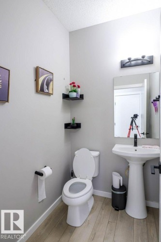 Well-appointed bathroom featuring light wood-look flooring, a white pedestal sink with a black faucet, and a toilet - 266 Charlesworth Drive, Edmonton, AB - Indoor Photo Showing Bathroom