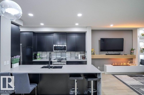 The kitchen features dark cabinetry, a light-colored countertop, and a tiled backsplash, with an integrated sink and modern faucet - 266 Charlesworth Drive, Edmonton, AB - Indoor