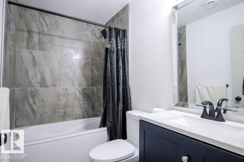 The bathroom features a white bathtub with tile surround, a dark vanity with a white countertop and sink, and a large mirror - 266 Charlesworth Drive, Edmonton, AB - Indoor Photo Showing Bathroom