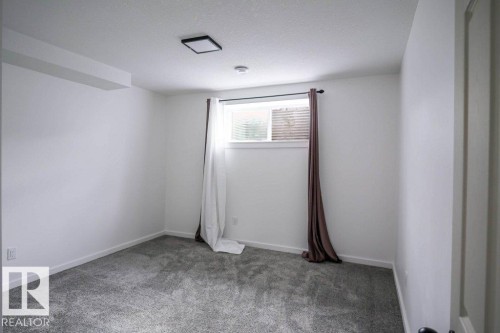 The room features light gray carpeting, white walls, and a window with blinds and dark-colored curtains - 266 Charlesworth Drive, Edmonton, AB - Indoor Photo Showing Other Room