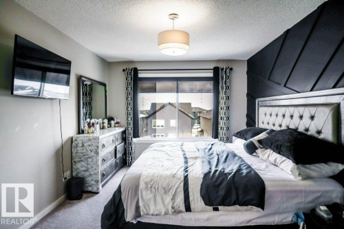 This bedroom features carpeted flooring, a decorative accent wall, and a large window with black and white patterned curtains - 266 Charlesworth Drive, Edmonton, AB - Indoor Photo Showing Bedroom
