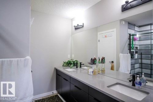 Bathroom featuring a dual vanity with a light-colored countertop, dark cabinetry, and integrated sinks - 266 Charlesworth Drive, Edmonton, AB - Indoor Photo Showing Bathroom