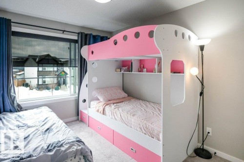 This room features light grey carpeting, a large window with privacy blinds and blue curtains, and light-colored walls - 266 Charlesworth Drive, Edmonton, AB - Indoor Photo Showing Bedroom