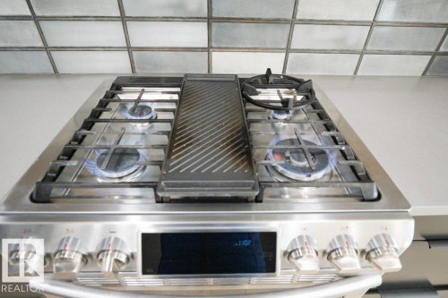 Modern stainless steel gas range with a built-in griddle, four burners, and control knobs, set against a tiled backsplash and light-colored countertop - 266 Charlesworth Drive, Edmonton, AB - Indoor Photo Showing Garage